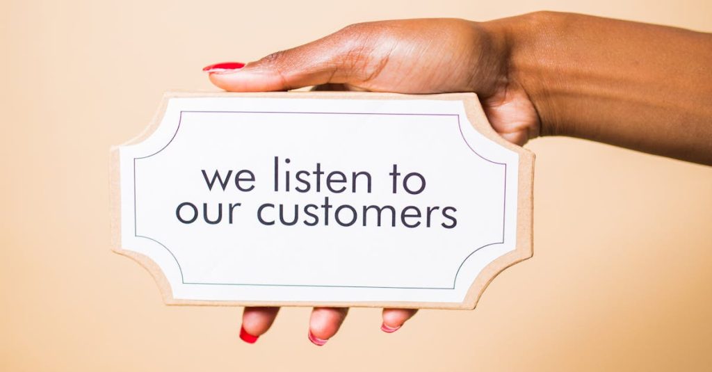 pexels-photo-7564196-7564196 A hand holding a sign saying 'we listen to our customers' on a neutral background.